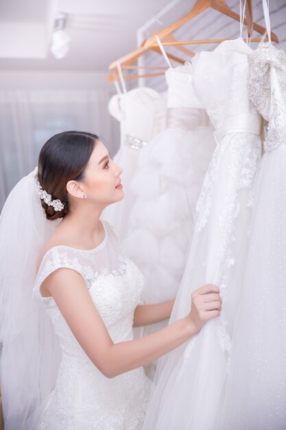 Sposa asiatica della giovane donna che prova sul vestito da sposa alle nozze moderne