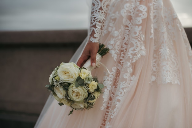 Sposa che indossa un bellissimo abito da sposa e tiene il mazzo di rose del giorno delle nozze