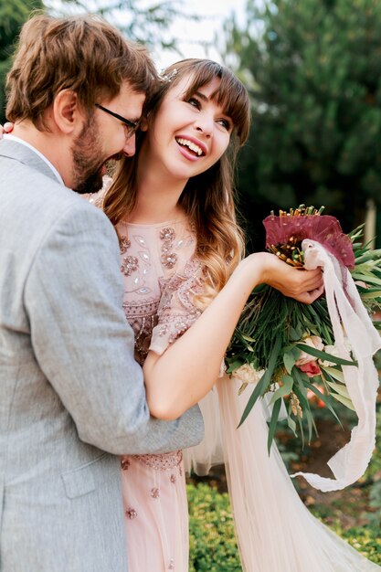 Sposa e sposo al giorno delle nozze camminando all'aperto sulla natura primaverile. Newlywed felice donna e uomo che abbracciano nel parco verde. Coppia di innamorati matrimonio.