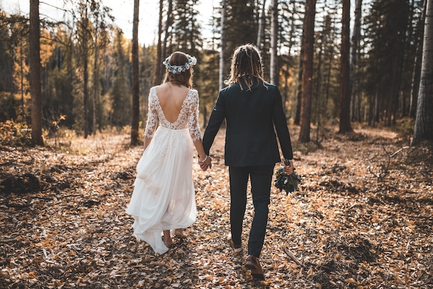 Sposa e sposo che camminano sulle foglie hanno coperto il terreno nei boschi durante il giorno