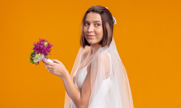 Sposa felice ed eccitata in un bellissimo abito da sposa che sta per lanciare un bouquet di fiori da sposa