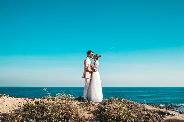 sposi in posa sulla scogliera dietro cielo blu e mare