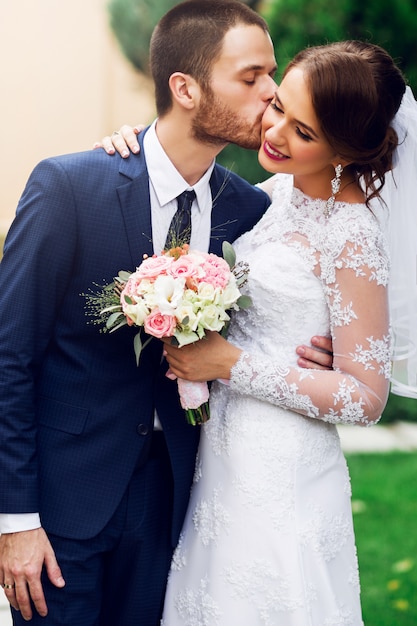 Sposi innamorati baci e sorridenti. Giovane sposa abbastanza elegante e il suo bel sposo in posa nel verde del parco.