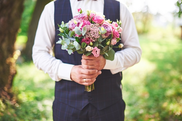 Sposo alla moda che tiene un bouquet da sposa rosa tenero.