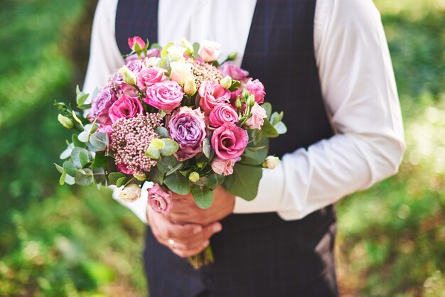 Sposo alla moda che tiene un bouquet da sposa rosa tenero.