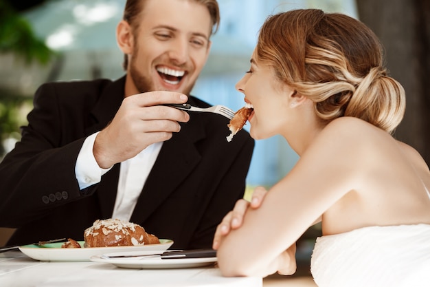 Sposo bello che alimenta la sua sposa di croissant in caffè.