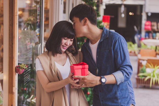 Sposo dando la sua fidanzata un regalo rosso e baciandola sulla fronte
