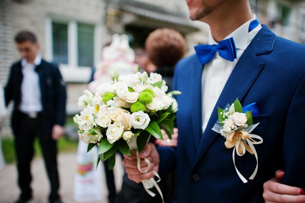 Sposo in giacca blu e papillon con bouquet