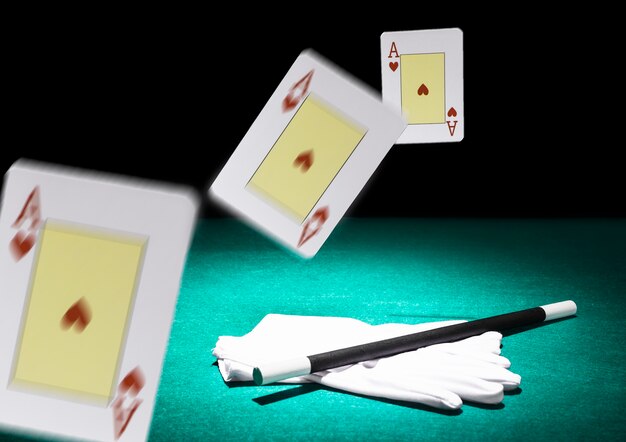Spostamento di tre carte da gioco in aria sopra il paio di guanti bianchi e bacchetta su sfondo verde