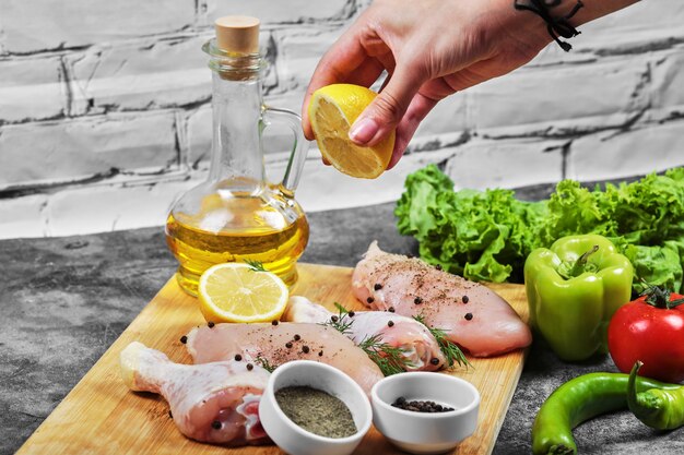 Spremere a mano il limone fresco sul piatto di carne di pollo cruda con un mazzo di verdure.