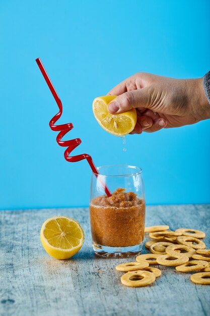 Spremere il limone fresco in un bicchiere di succo con paglia e cracker sul tavolo grigio.