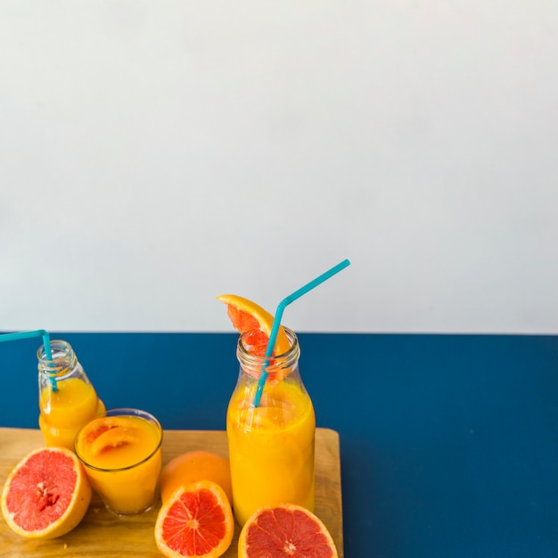 Spremuta di pompelmo con cannuccia e frutta sul tagliere contro fondo blu