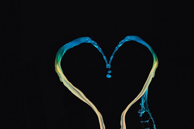 Spruzzi acquerello blu e giallo che formano a forma di cuore su sfondo nero