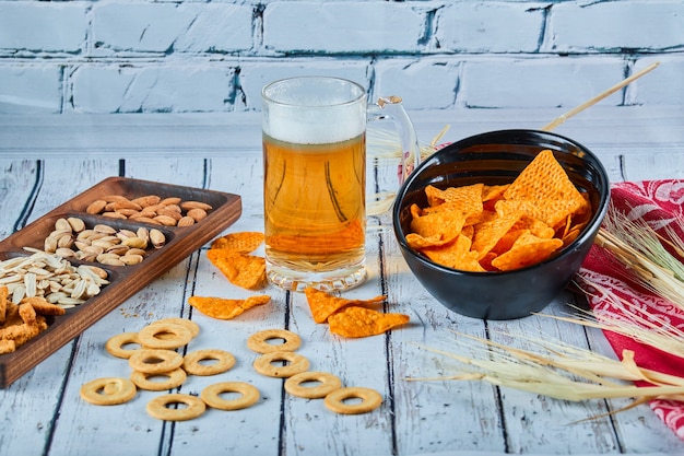 Spuntini assortiti, patatine e un bicchiere di birra sul tavolo blu.