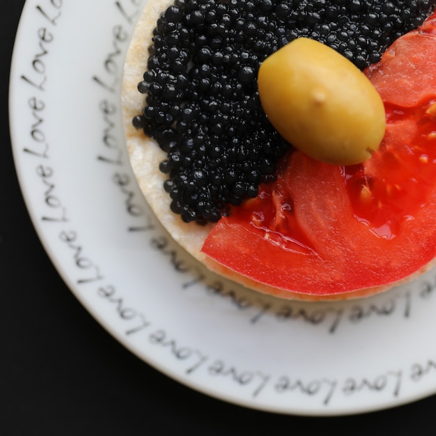 Spuntino con pomodoro, caviale nero e un'oliva.