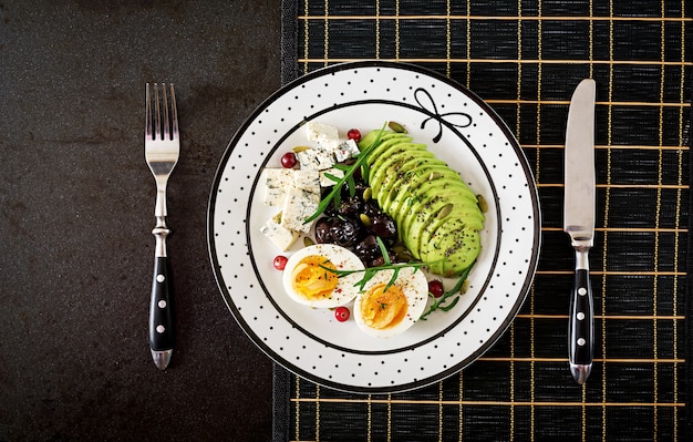 Spuntino o colazione sana - piatto di gorgonzola, avocado, uovo sodo, olive su una superficie nera. Vista dall'alto