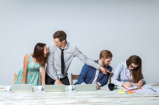 Squadra di affari che lavora al loro progetto di affari insieme all'ufficio su sfondo grigio chiaro. tutti sorridendo e guardando il capo. il capo sta scrivendo su un taccuino. immagine copyspace.