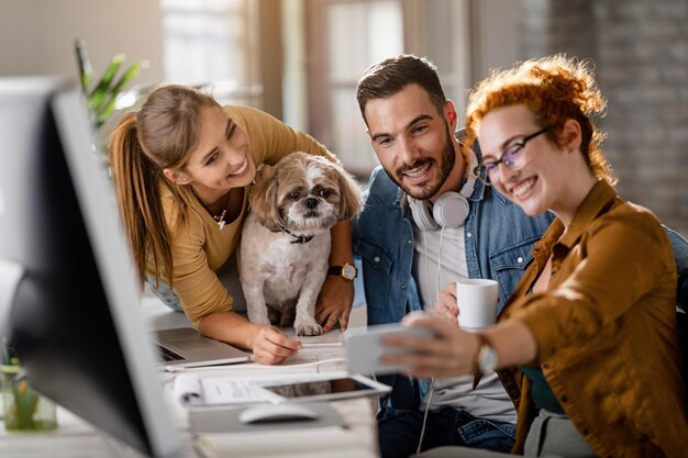 Squadra di allegri colleghi di lavoro con un cane che si diverte mentre si fa selfie in ufficio