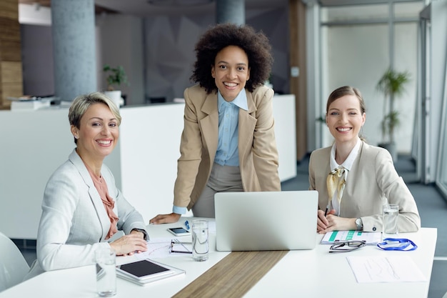 Squadra di donne d'affari felici che lavorano in ufficio e che guarda l'obbiettivo