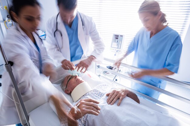 Squadra di medici che mettono la maschera di ossigeno su un fronte paziente senior maschio