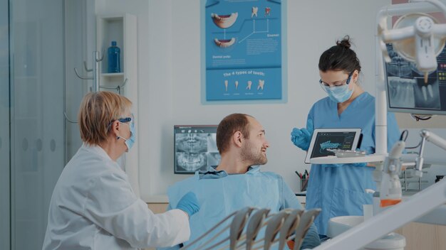 Squadra di odontoiatria che spiega la radiografia al paziente malato, facendo un esame di igiene orale per curare il mal di denti. Stomatologo e assistente che consultano i risultati dei raggi x per eseguire la procedura di trapano dentale.