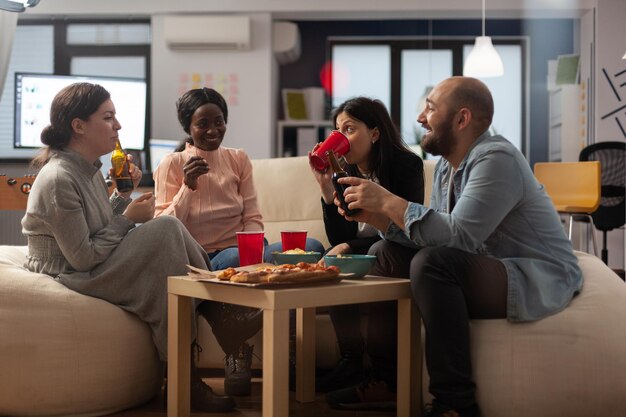 Squadra eterogenea di colleghi che si incontrano per un drink in ufficio dopo il lavoro, divertendosi con birra e snack a base di pizza. Compagni di lavoro che si divertono e discutono con l'alcol dopo l'orario di lavoro.