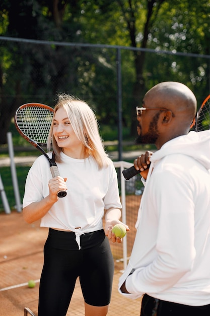 Stagione estiva. Giovane ragazzo nero con racchetta e ragazza che conversano al parco giochi. Tennis, hobby.