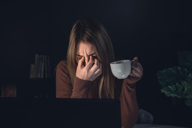 Stanco giovane donna che lavora dietro un computer portatile di notte occhi malati