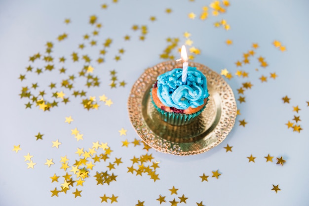 Stelle sparse attorno alla candela illuminata sopra il cupcake sul piatto d&#39;oro