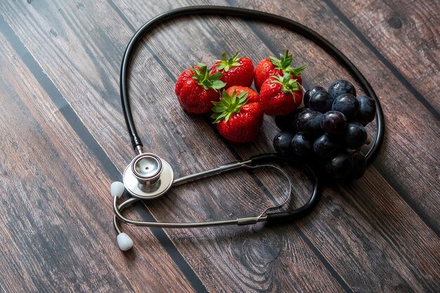 Stetoscopio con fragole e uva nera senza semi sulla parte superiore del tavolo in legno.