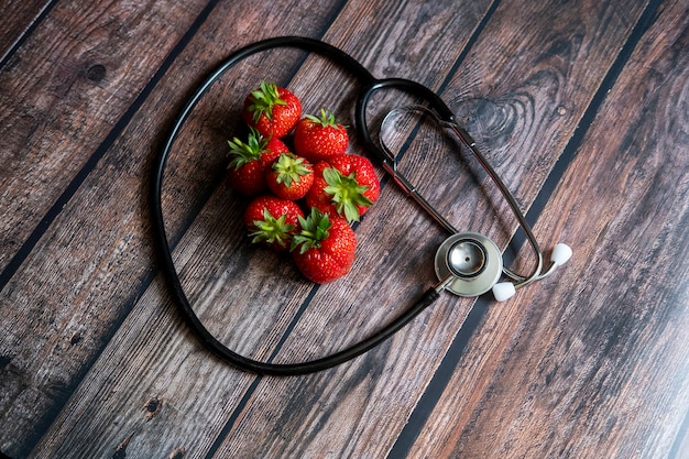 Stetoscopio con fragole in cima al tavolo di legno. Concettuale medico e sanitario.