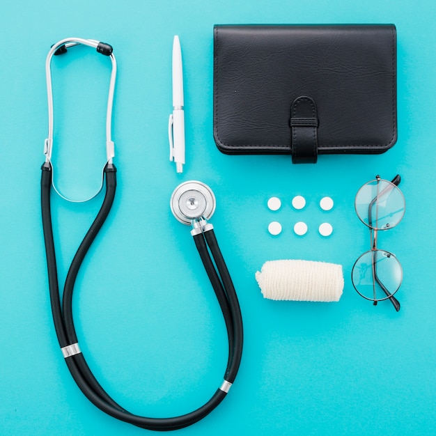 Stetoscopio; penna; pillole; diario; occhiali e benda su sfondo blu
