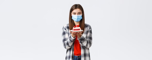 Stile di vita dell'epidemia di coronavirus durante l'allontanamento sociale e il concetto di celebrazione delle vacanze Giovane donna carina in maschera medica che celebra il compleanno da solo durante la quarantena, tenere la torta di compleanno