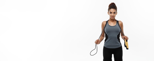 Stile di vita di formazione sportiva e concetto di fitness Ritratto di bella donna afroamericana felice che si esercita con la corda per saltare isolato su sfondo bianco per studio