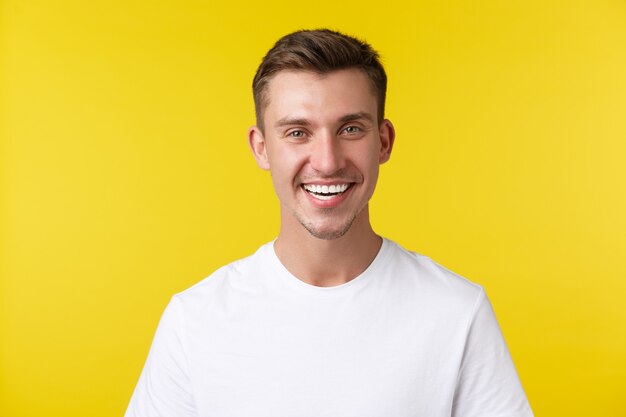 Stile di vita, estate e concetto di emozioni delle persone. Entusiasta bel modello maschile con sorriso felice e denti bianchi, in piedi in maglietta casual su sfondo giallo soddisfatto.