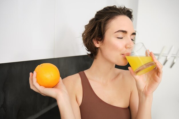 Stile di vita sano e sport bella donna sorridente che beve succo d'arancia fresco e tiene la frutta dentro