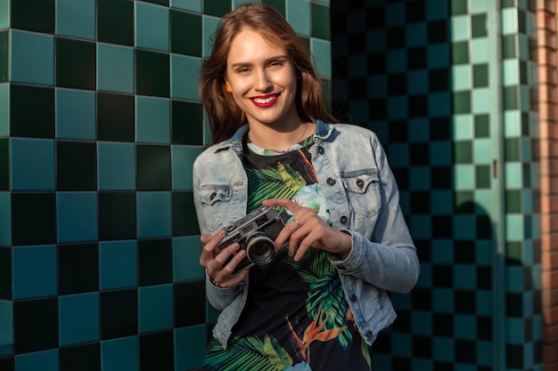 Stile di vita soleggiato ritratto di moda di giovane donna alla moda che cammina per strada, con la fotocamera, sorridente, goditi i fine settimana, fai una foto del suo viaggio, vecchia fotocamera retrò, vintage