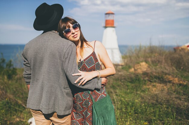 Stile indie delle coppie giovani hipster nell'amore che cammina nella campagna, faro sullo sfondo