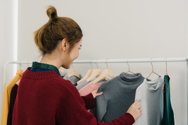 Stilista femminile asiatico che lavora, che controlla e che sceglie i vestiti