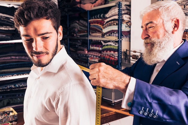 Stilista maschio senior che prende misura del suo cliente nel negozio