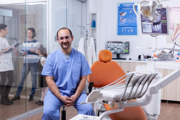 Stomatolog nella clinica dei denti professioanl sorridente indossando l'uniforme che guarda l'obbiettivo. Medico dentista che discute con la madre e il bambino sul trattamento dei denti.