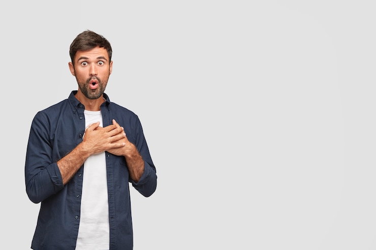Foto gratuito stordito uomo emotivo con la barba lunga con espressione scioccata, tiene entrambi i palmi sul cuore, vede qualcosa di fantastico di fronte
