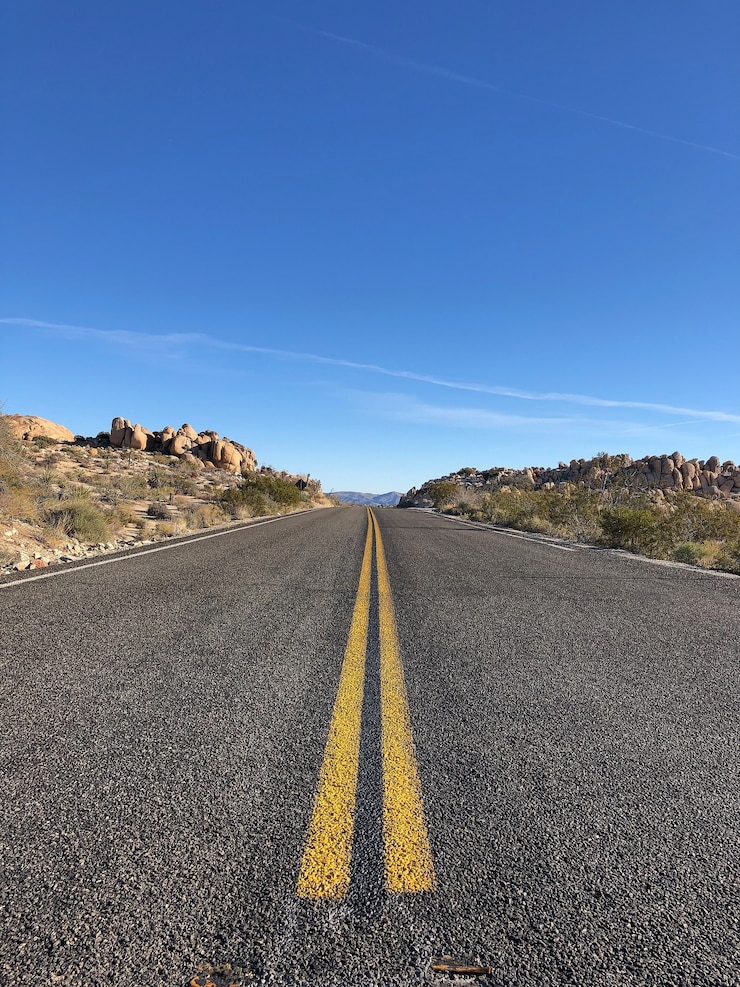 Foto gratuito strada asfaltata con linee gialle sotto un cielo blu chiaro