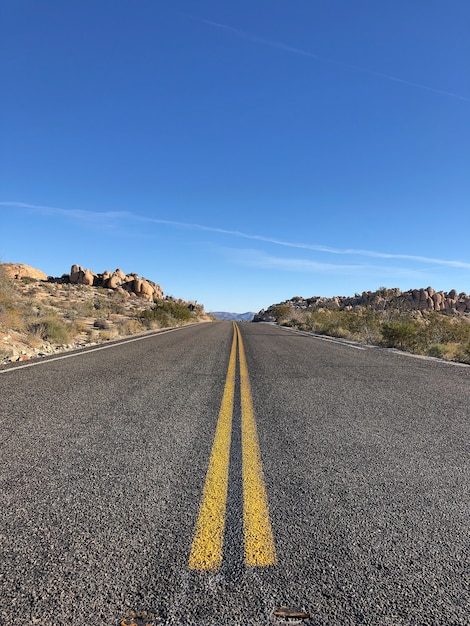 Strada asfaltata con linee gialle sotto un cielo blu chiaro