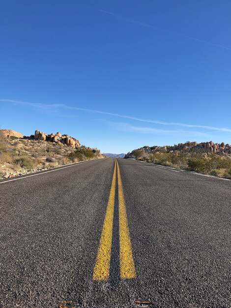 Strada asfaltata con linee gialle sotto un cielo blu chiaro