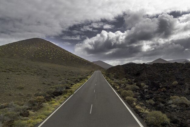 Strada circondata da colline sotto un cielo nuvoloso nel Parco Nazionale di Timanfaya in Spagna