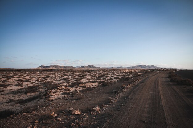 Strada non asfaltata vicino ad un campo secco con le montagne nella distanza e nel chiaro cielo blu