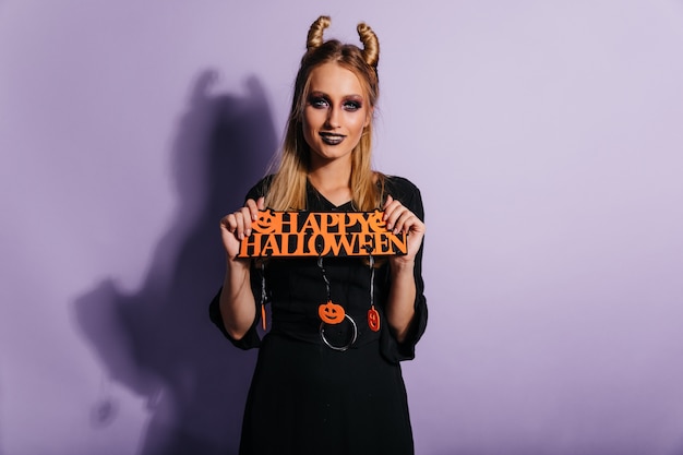 Strega cattiva in vestito nero lungo che gode della festa. Ragazza caucasica che celebra halloween.