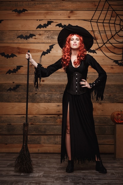 Strega di Halloween concetto integrale felice halloween strega capelli rossi che tiene in posa con scopa magica...