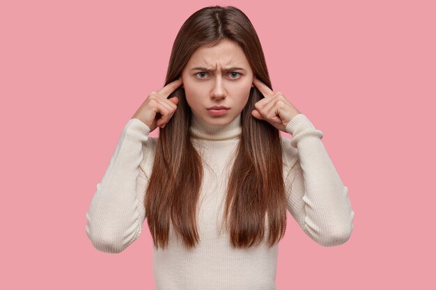 Stressante donna caucasica infelice ignora qualcosa di spiacevole, tappi le orecchie, infastidita da un forte rumore, aggrotta le sopracciglia, ha un'espressione cupa